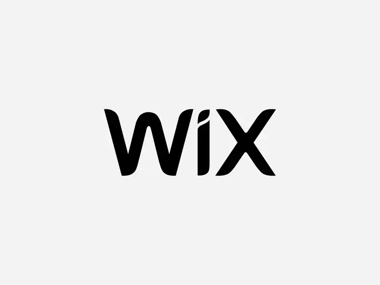 Przedsiębiorca siedzący przy czarnym biurku i zakładający sklep online na Wix na biurku znajduje się laptop z otwartą platformą eCommerce oraz czarny telefon i szary kubek Kobieta ubrana jest w elegancki ubiór marynarkę oraz posiada naszyjnik